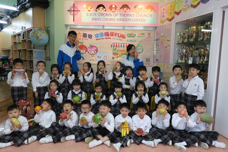 教师与学生手持各种水果在『开心果「月」』横额前拍照留念。
